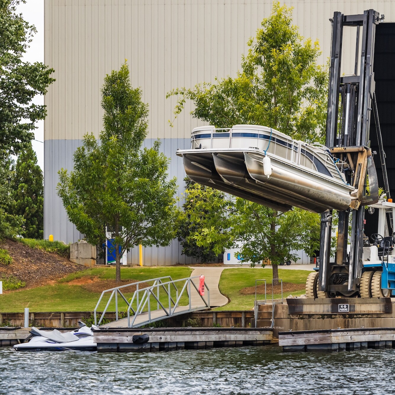 Pontoon boat removed from dry dock marina storage resting on fork lift ready for launch.